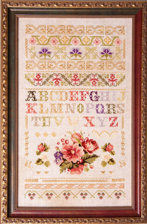 Decorative cross-stitch pattern with floral design and alphabet letters in a decorative frame.