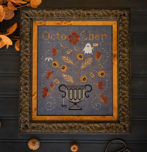 A framed cross-stitch design featuring an autumn scene with a white ghost, flowers, leaves, and a dark urn.  Glory Ghost design by Plum Street Samplers