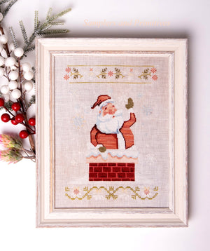 Framed cross-stitched picture of Santa Claus in a chimney with decorative elements.