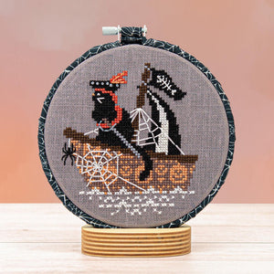 Cross-stitched design of a black cat in a boat with spider webs 